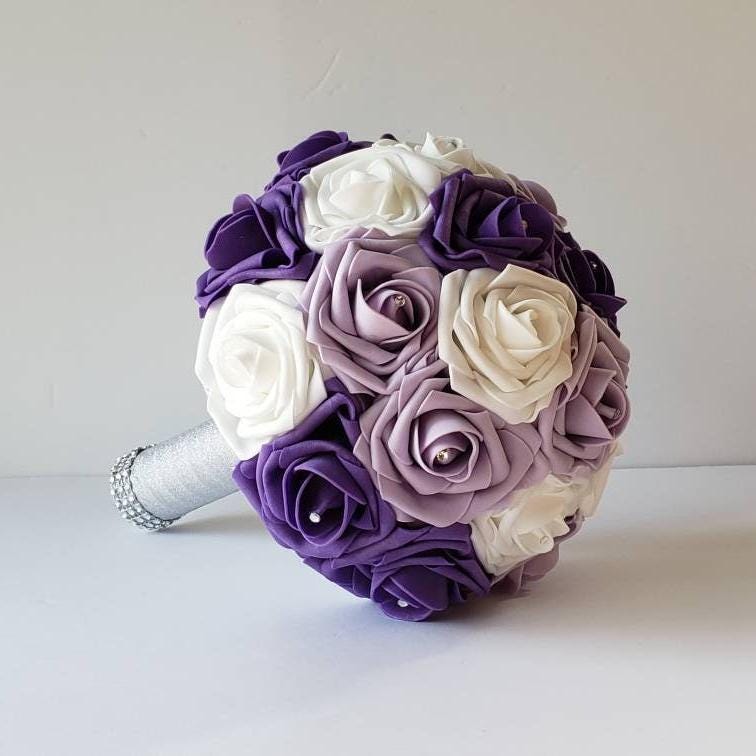 lilac, purple, and white bridal bouquet made with real touch roses. rhinestones are in the center of every rose. Handle is made with silver ribbon and finished with silver bling wrap.