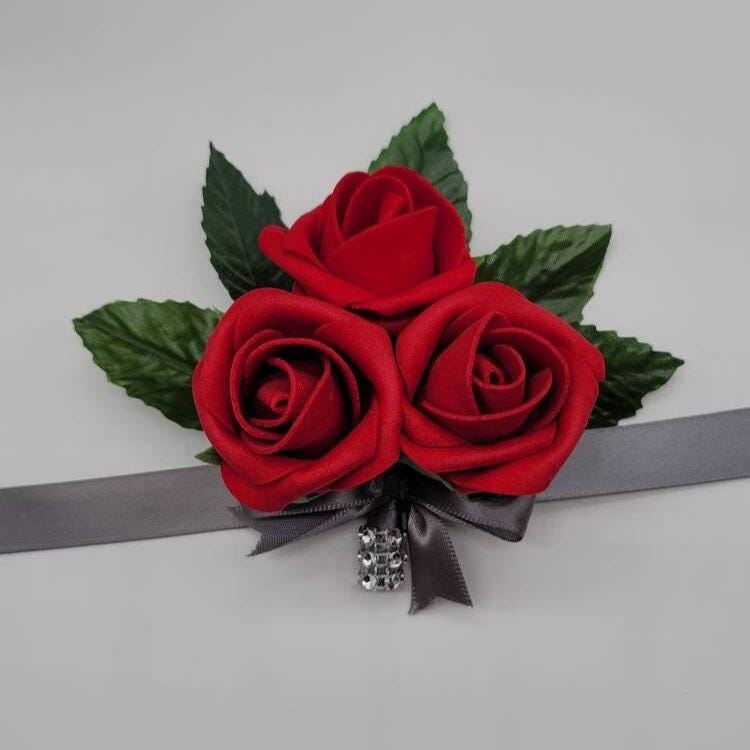 Red 3 rose wrist corsage with gray ribbon and a strip of silver bling wrap on handle.