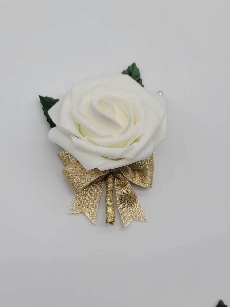 May include: A single white foam rose with a gold bow and green leaves. The rose is attached to a brown stem.