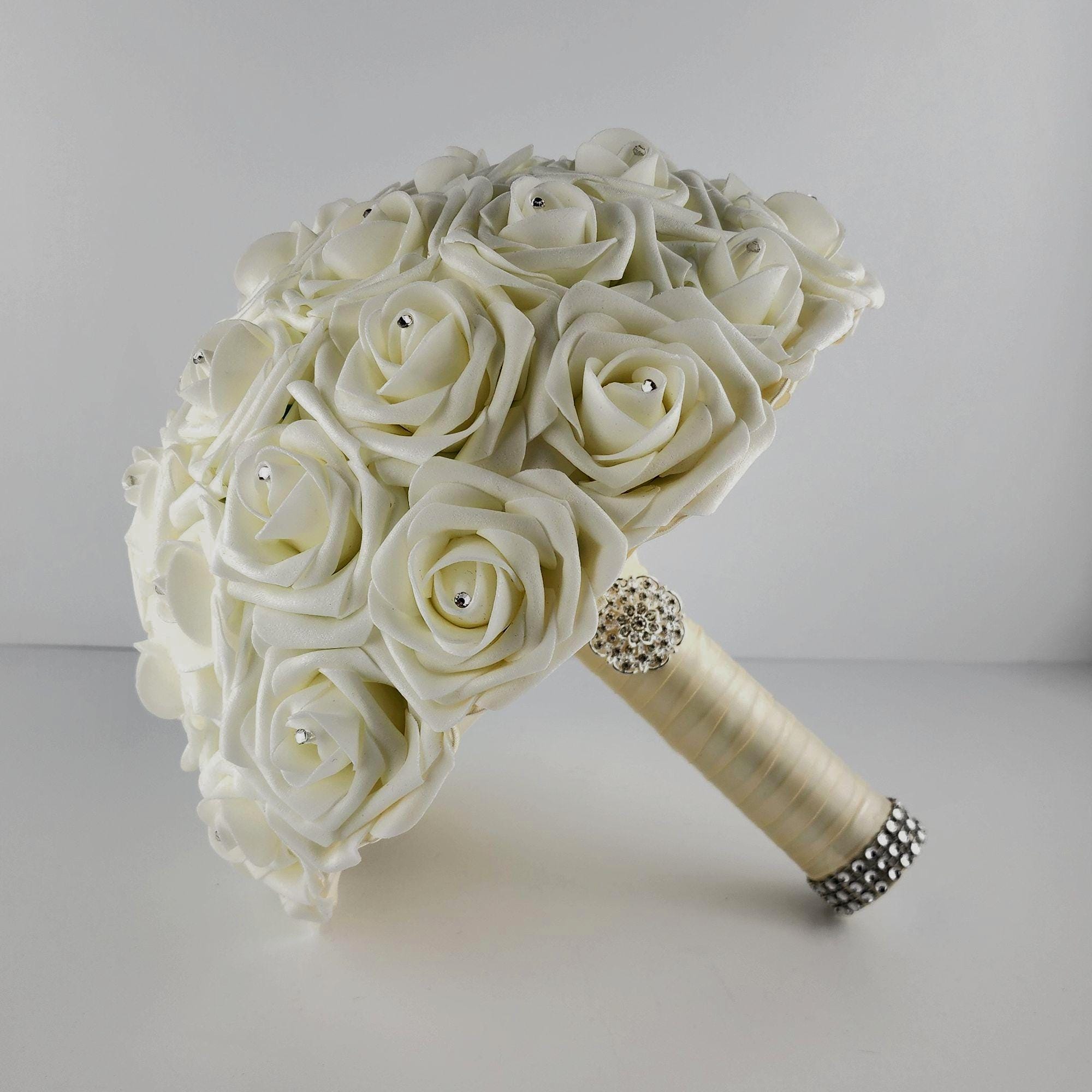 Ivory roses with rhinestones on every rose. Handle is made out of ivory satin ribbon and finished with silver bling wrap.