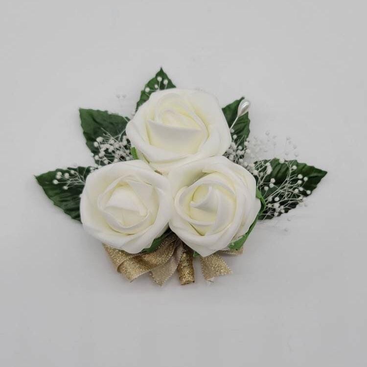 Ivory pin on corsage with gold ribbon and baby's breath.