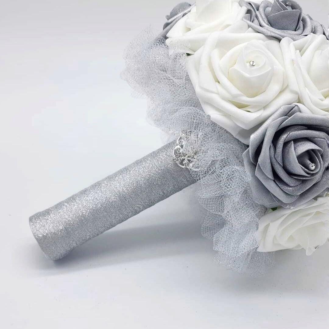 A silver and white bridal bouquet with a silver glitter handle and a rhinestone brooch. The bouquet is made of real touch roses and tulle.