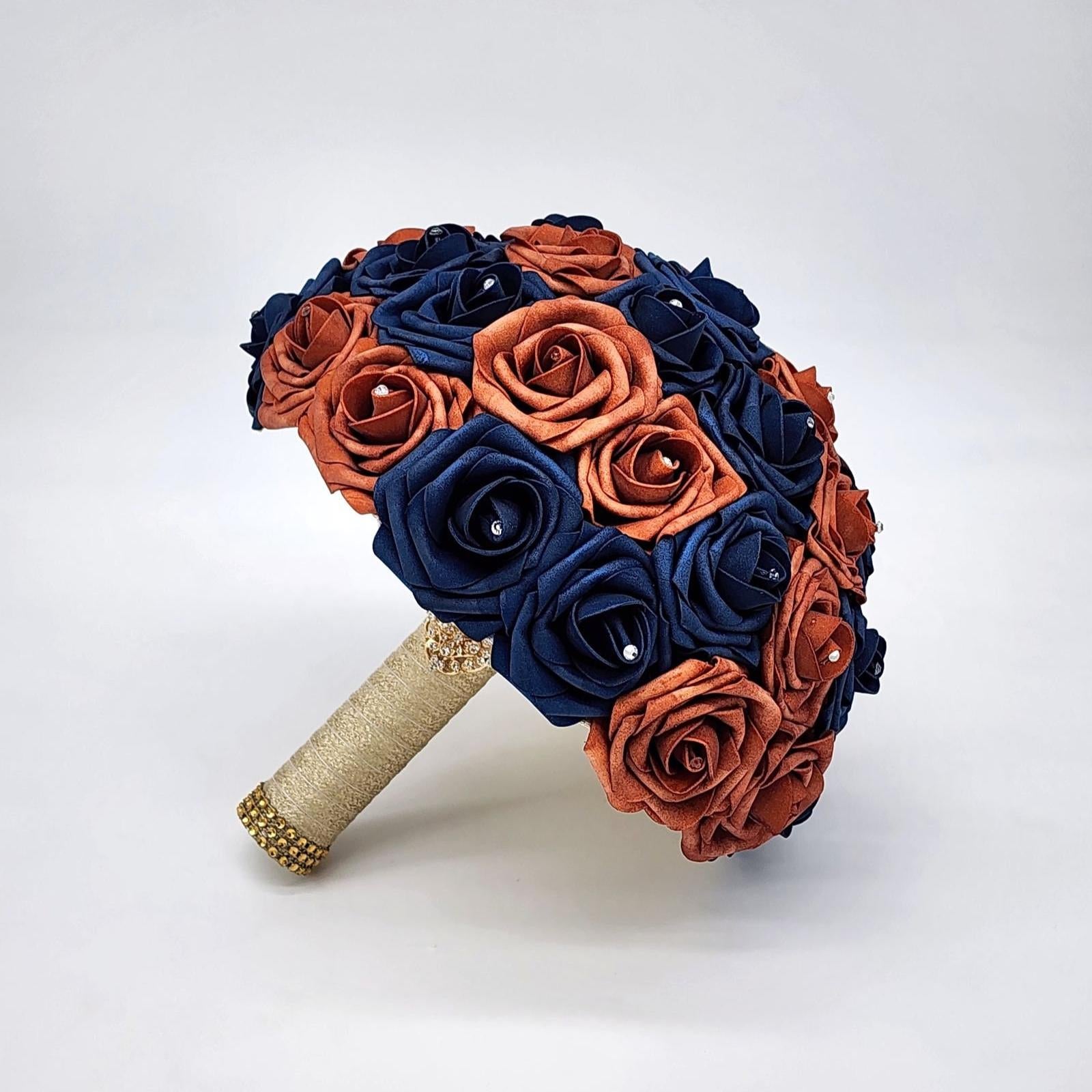 A bridal bouquet made of Real Touch roses in navy blue and burnt orange. The bouquet has a gold ribbon and is decorated with rhinestones.